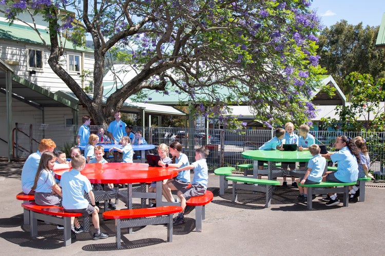 Three groups of students sitting around tables outside in playground.