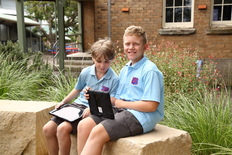 Two stdents sitting outside working on ipads.