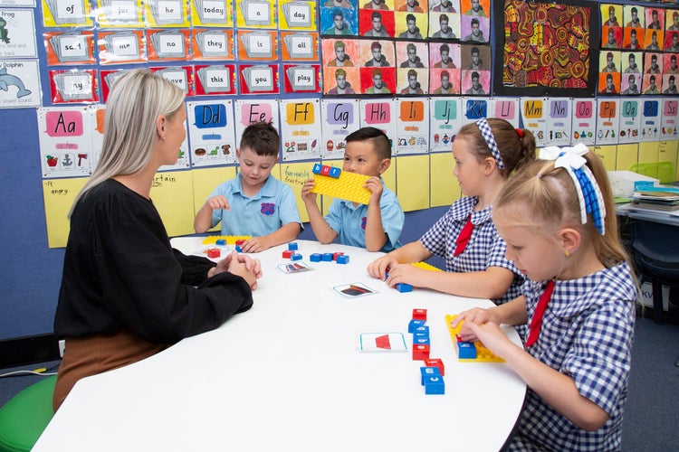 Teacher sitting in class with students working at a desk.