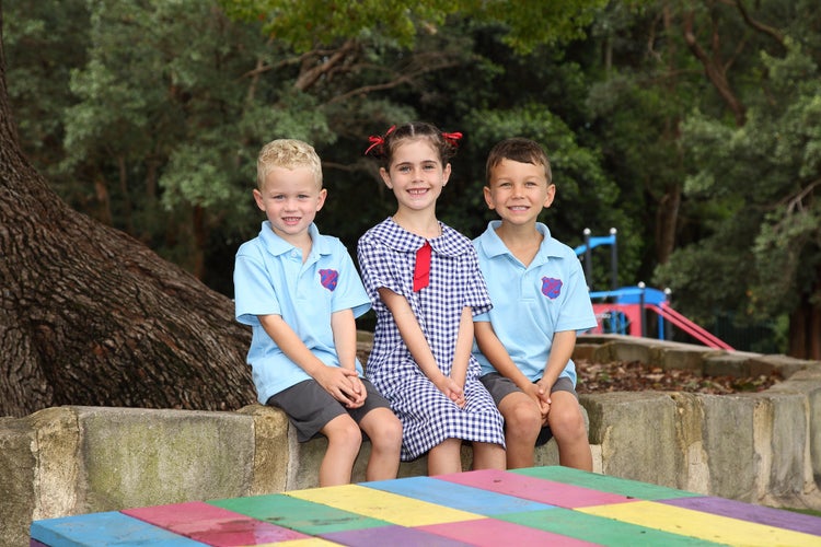 Three students sitting in playground smiling for photo.