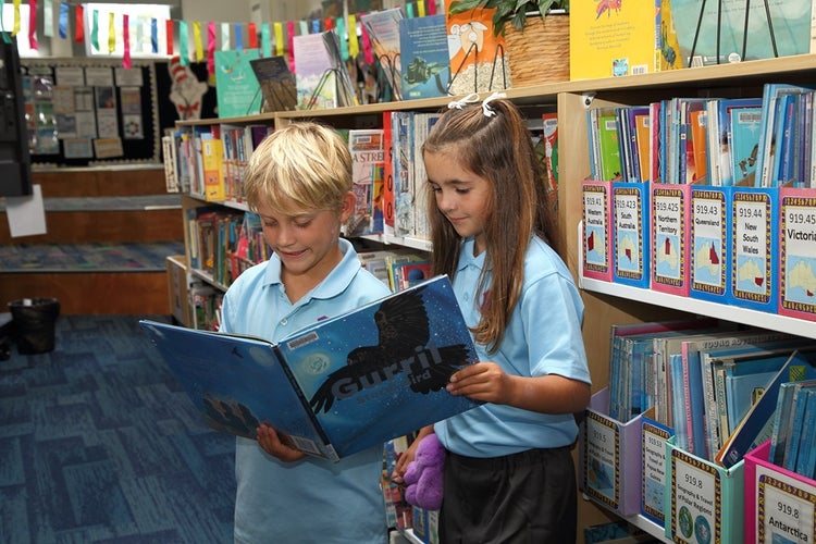 Two students looking at an open book in the library.